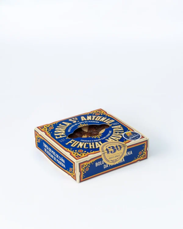 Caixa de Bolo de Mel de Cana da Fábrica Santo António, versão mais pequena, vista em ângulo, tons de azul e dourado com janela recortada