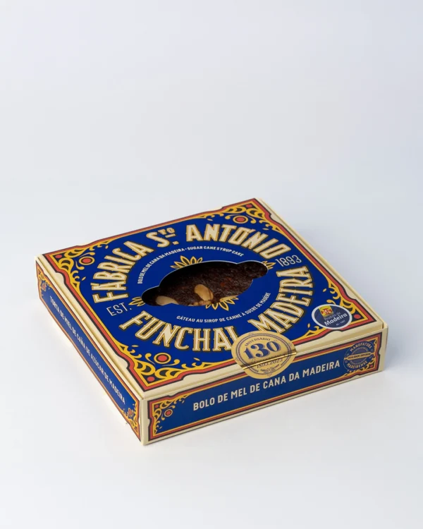 Caixa de Bolo de Mel de Cana da Fábrica Santo António, vista em ângulo, tons de azul e dourado com janela recortada