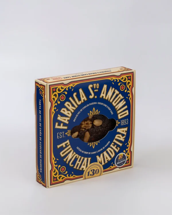 Caixa de Bolo de Mel de Cana da Fábrica Santo António, embalagem em tons de azul e dourado com janela recortada mostrando o bolo com pedaços de noz e amêndoa, sobre fundo branco