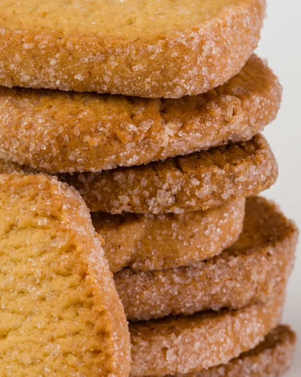 Bolachas douradas Caramelini da Fábrica Santo António, close-up empilhadas, rebordo com cristais de açúcar visíveis