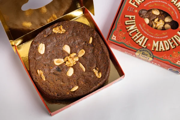 Bolo de Mel de Cana da Madeira, edição de Natal, vista de cima, pedaços de noz, amêndoa e passas visíveis, caixa fechada ao lado